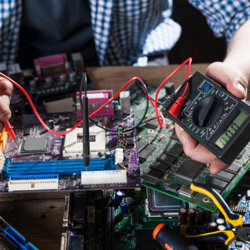 Technician measuring a motherboard with a multimeter during fault finding.