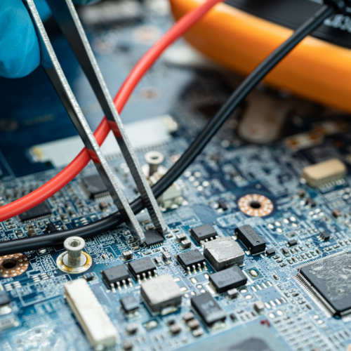Close-up of motherboard component work with tweezers and a multimeter.